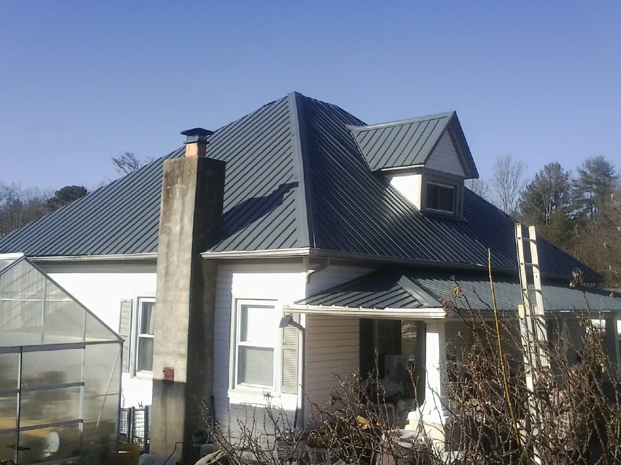 Dark blue standing seam metal roof on a white farmhouse with dormer — Slate & Tile Roof Repair by Roofing Brothers in Thompsonville