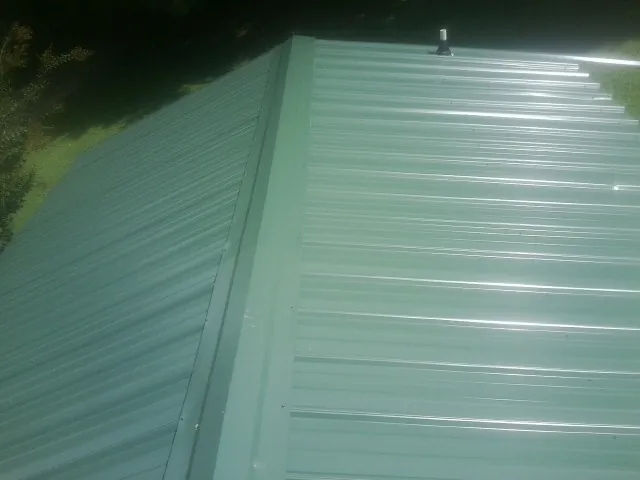 New green metal panels meeting at the ridge of a roof — Flat Roof Repair work by our crew in Thompsonville