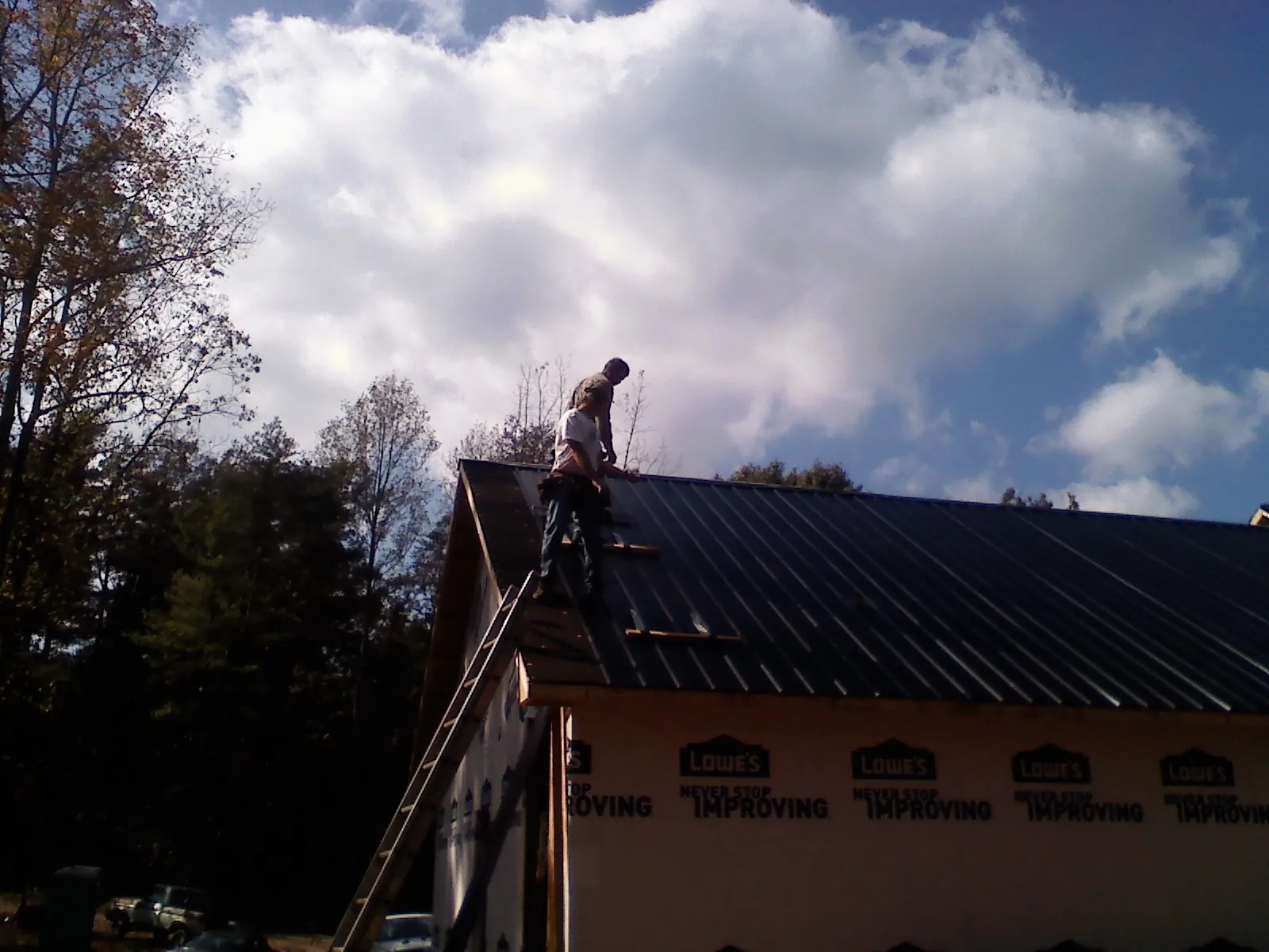 Roofer fastening dark metal panels high against a cloudy sky, from a Roof Inspection job in Thompsonville