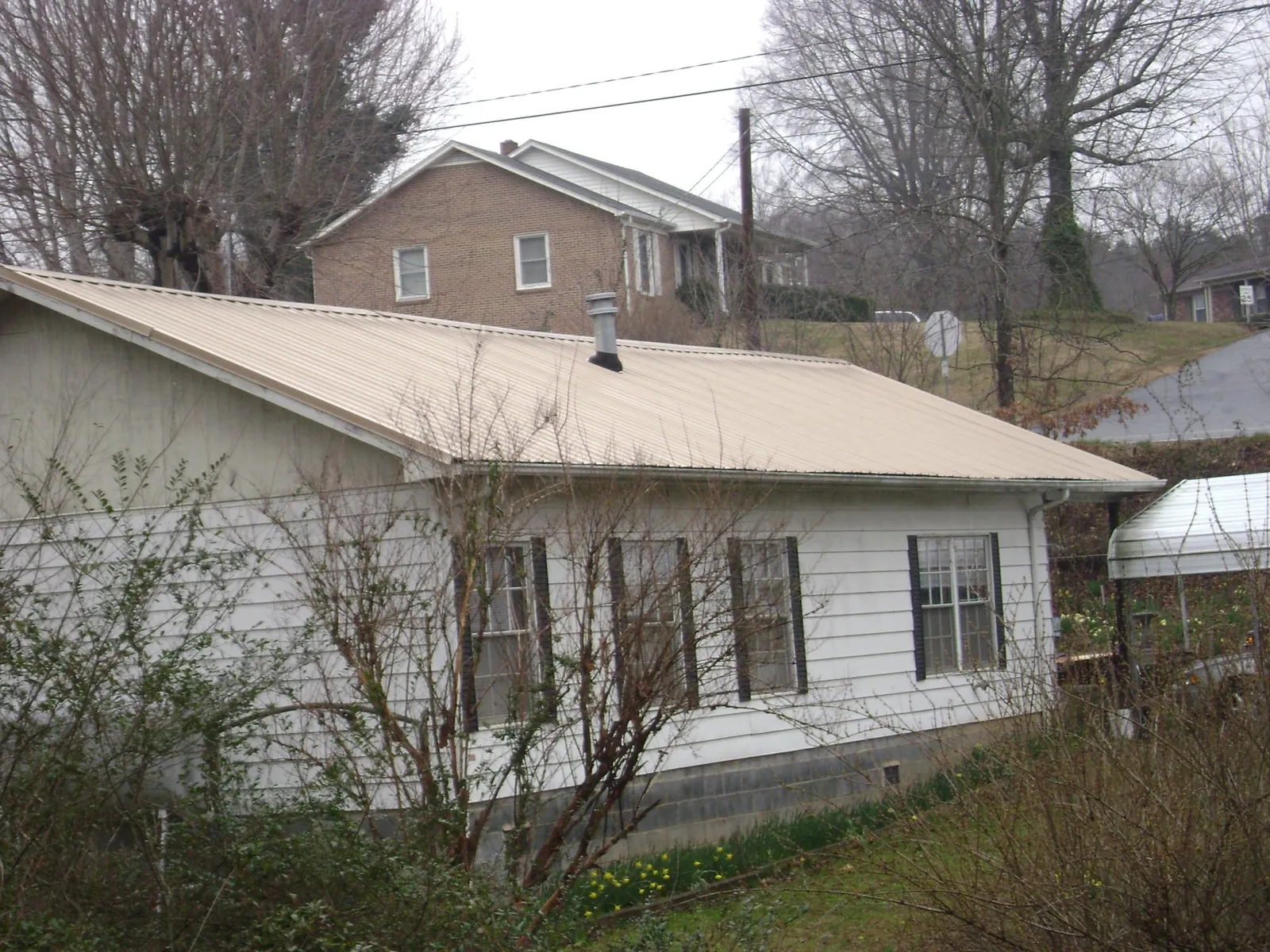 Tan metal roof on a white sided house set into a hillside — Commercial Roofing by Roofing Brothers in Thompsonville
